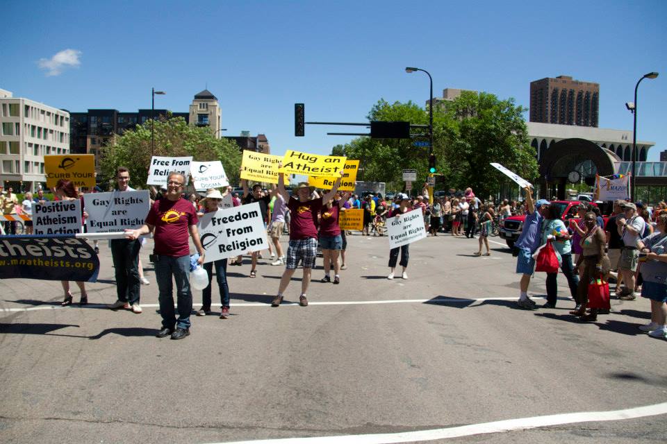 Wide shot of people marching behind Minnesota Atheist banner with handheld signs.
