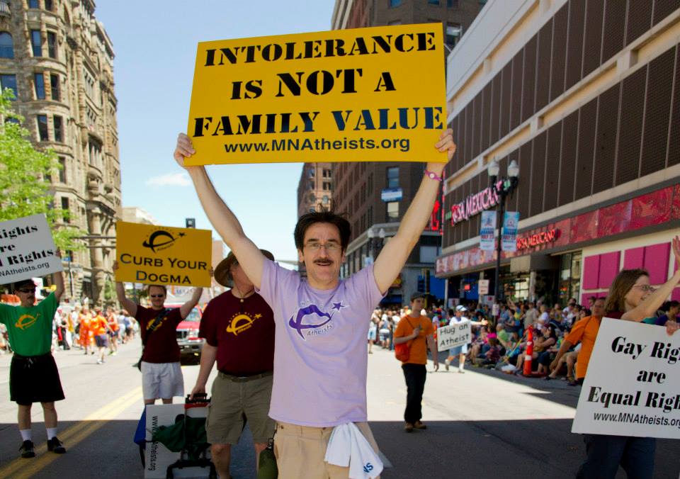 Group of people marching in parade with handheld signs reading, "Curb your dogma" and "Intolerance is not a family value."