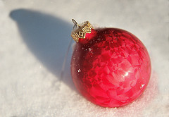 Photo of a bright red ball ornament sitting in the snow.