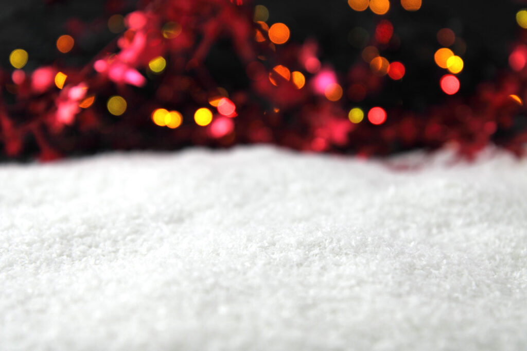 Photo of snow with colored lights out of focus in the background.