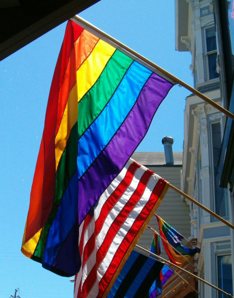 Photo of the rainbow pride flag flying next to the U.S. flag.