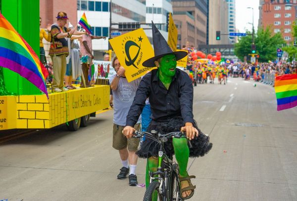 Photo of Dane at Pride as the Wicked With of the West on a bicycle.